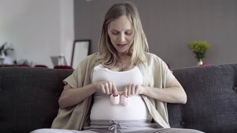 Vorderansicht-Einer-Schwangeren-Frau,-Die-Mit-Babyschuhen-Auf-Dem-Bauch-Spielt